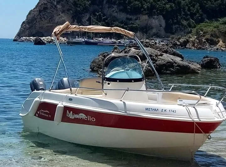 The Mistral on the water beside the rocks, with its sun canopy up.