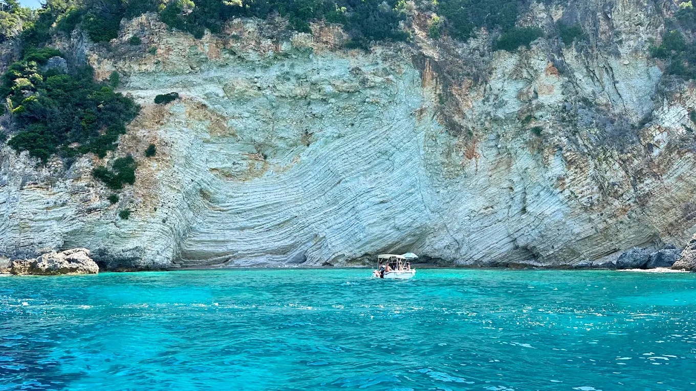 The Paleokastritsa coastline from the water — steep cliffs dropping into deep blue sea.