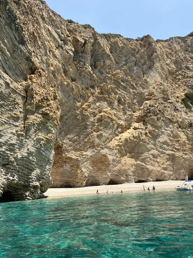 The pebble shore of Paradise Beach, known locally as Chomi, at the foot of tall limestone cliffs.
