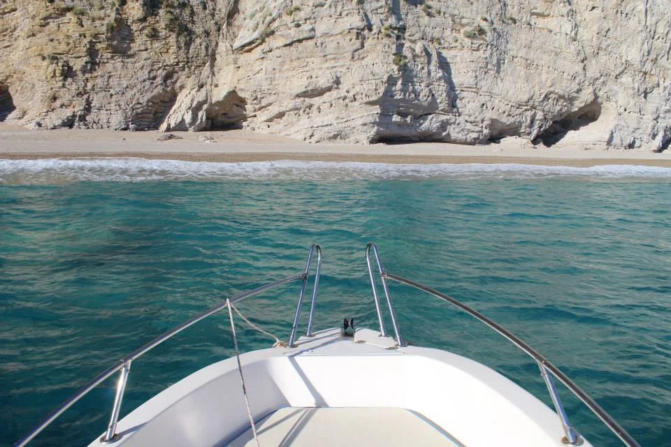 Stelari beach seen from the bow of a Capitano boat, with clear green water over the shallows.