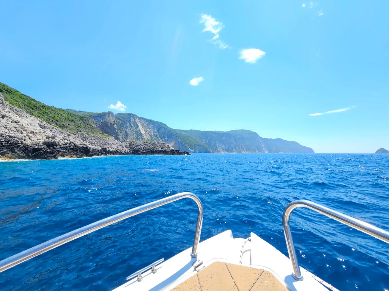 The view forward over the bow of a boat on open water, with the cliffs of the Paleokastritsa coast ahead.
