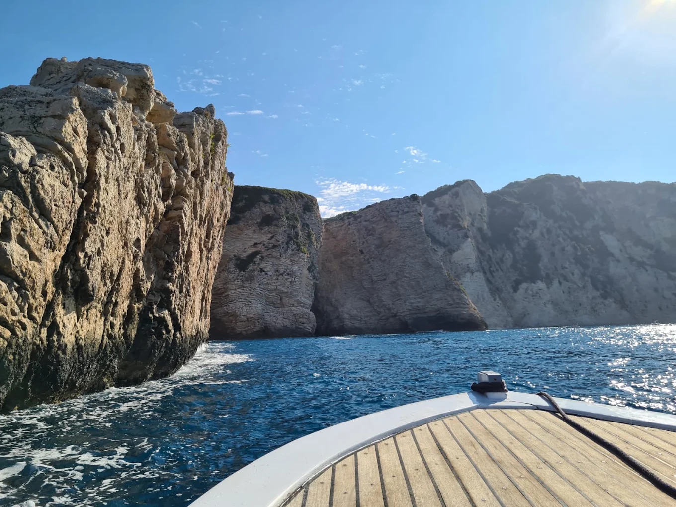 The bow of a boat heading into a channel between tall limestone cliffs on the Paleokastritsa coast.